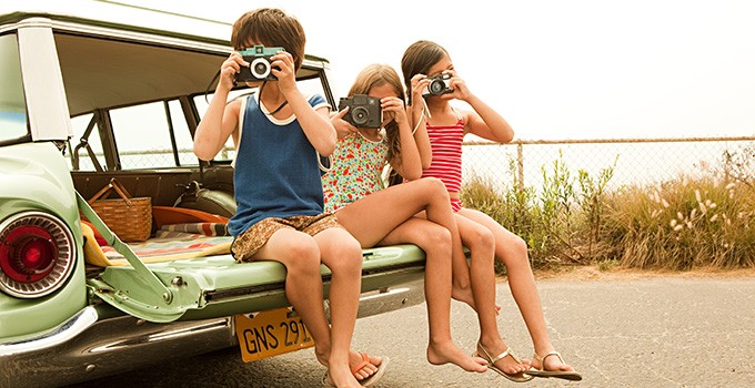 Three young kids, sitting on the back of a 1950's station wagon, taking photos.