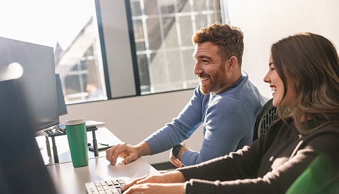 Happy young male and female coworkers sitting in the office looking at a computer screen together.