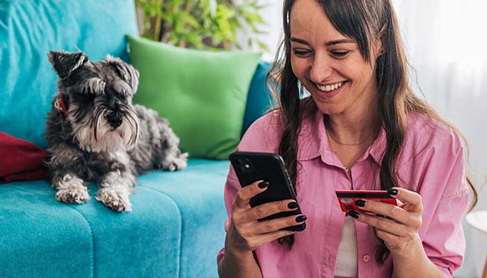 Young woman looking at her phone, while holding a credit card.